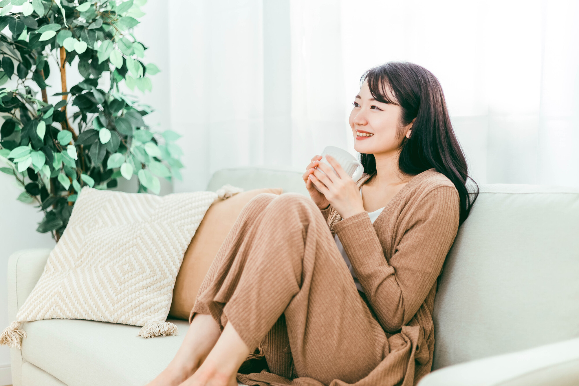 マグカップを手に持ち、部屋でホッとする女性