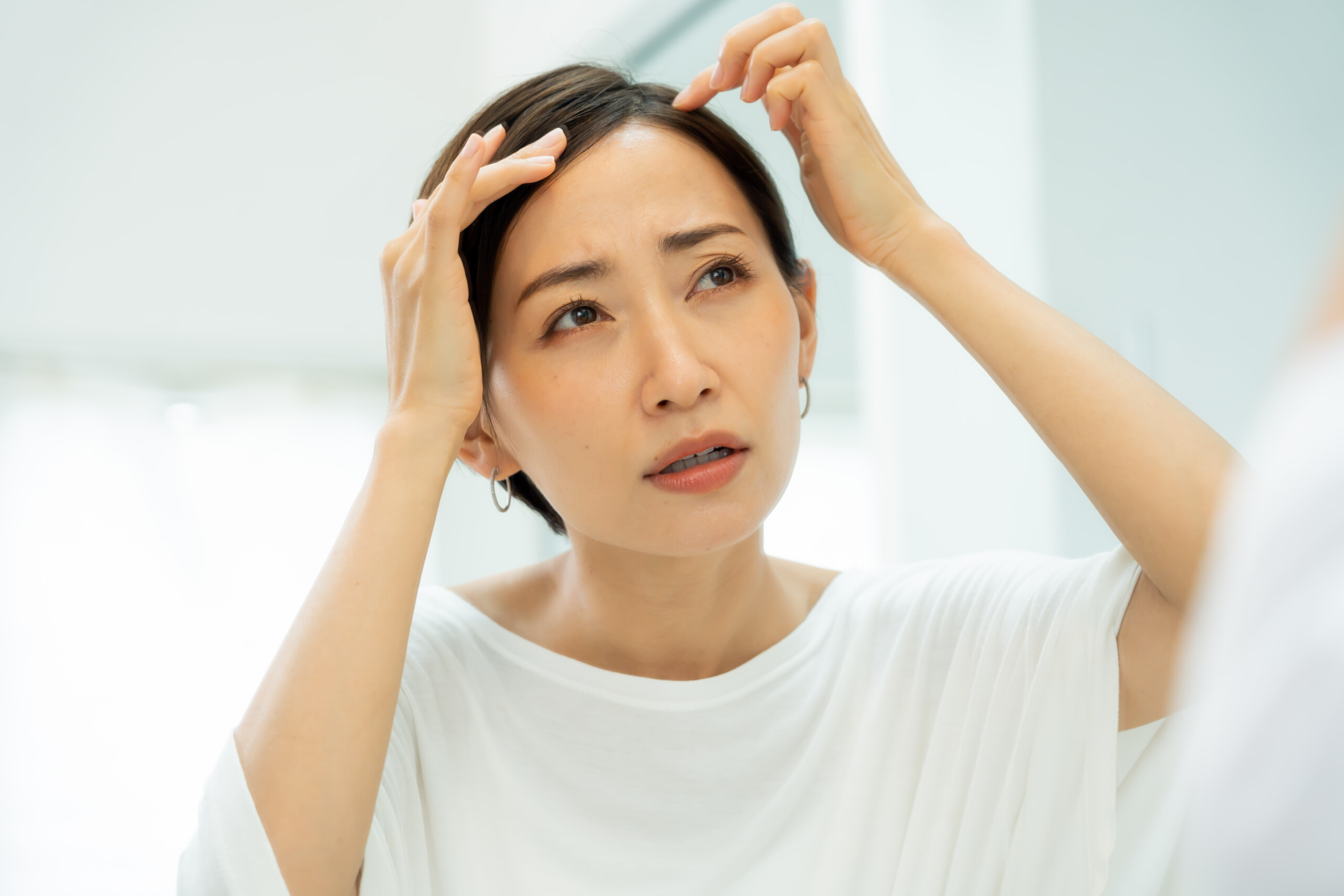 生え際を不安そうに見つめる女性