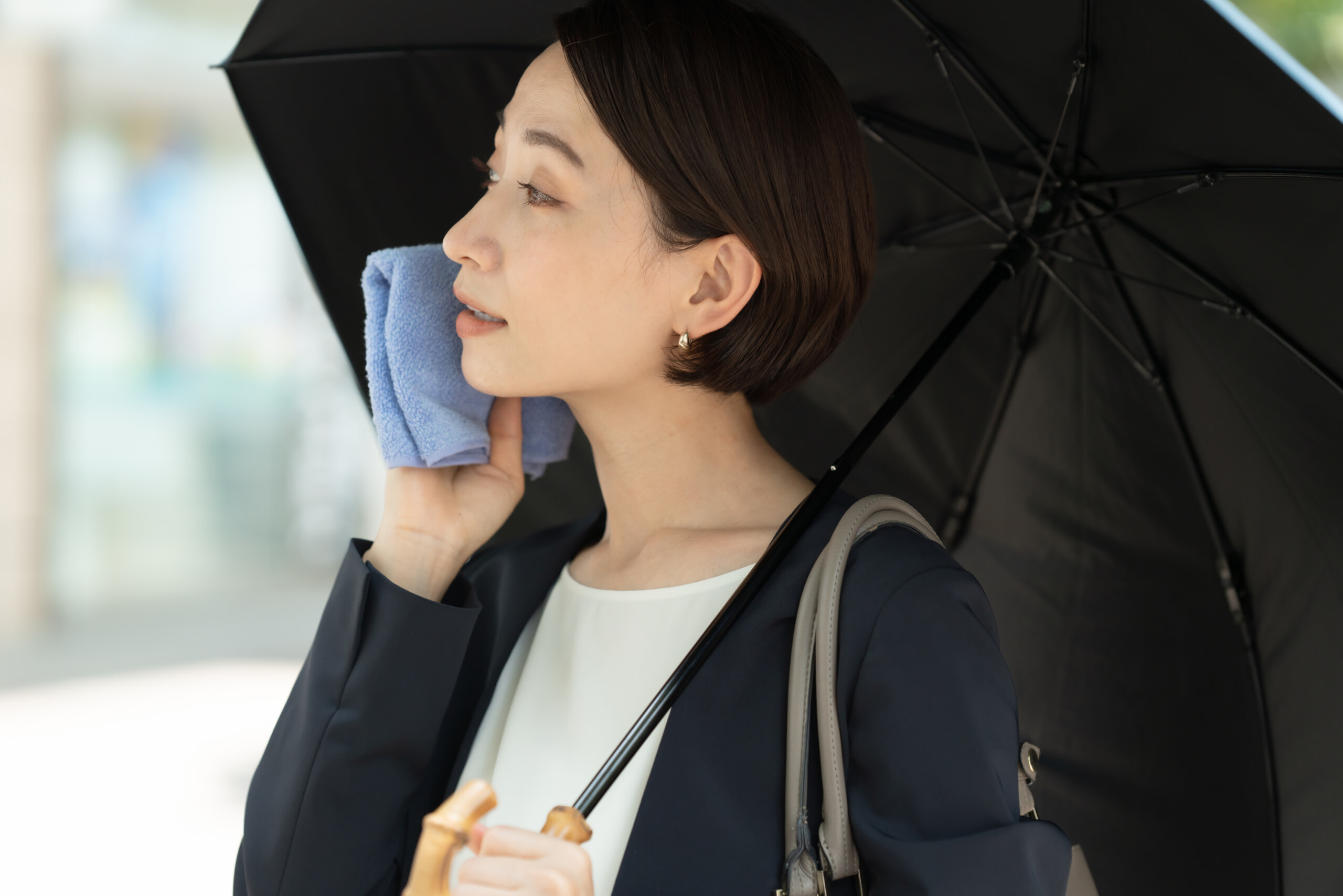 日傘をさしながら汗を拭く女性