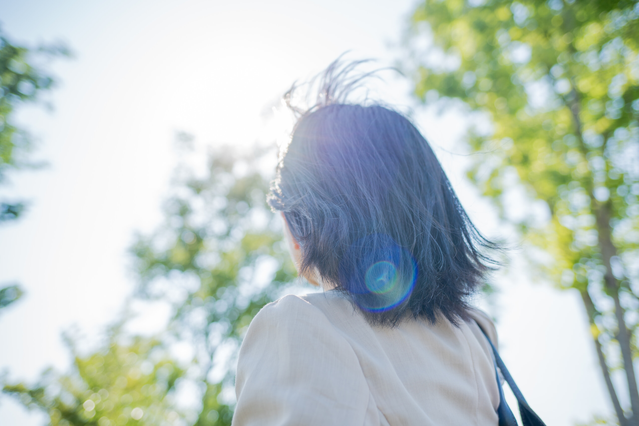 外で陽ざしを浴びる女性の後ろ姿